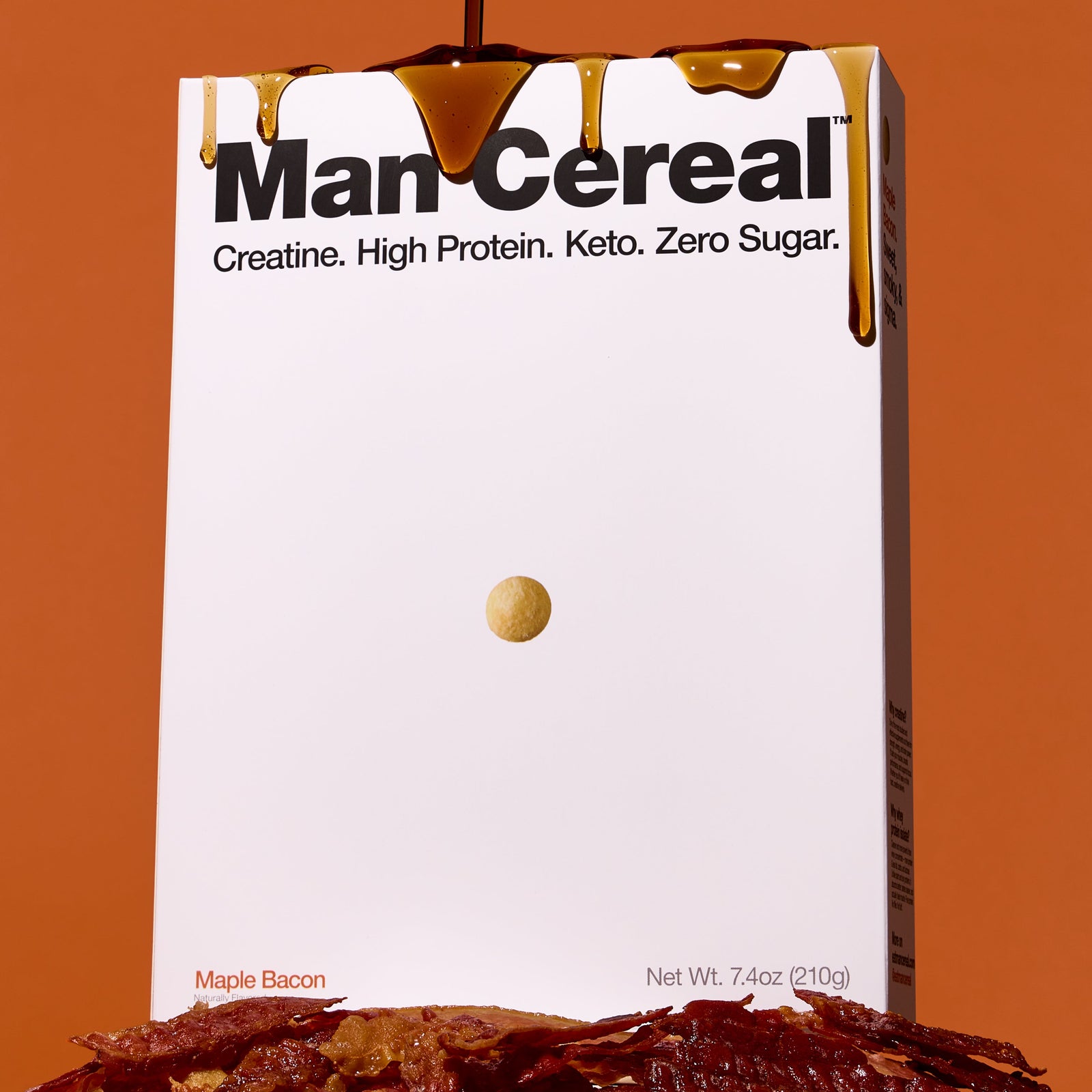 Box of 'Man Cereal' with a drizzle of syrup and bacon slices on an orange background
