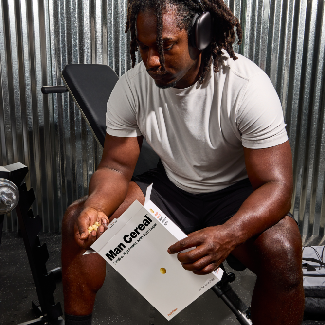 Man sitting on a weight gym bench holding a box of Man Cereal