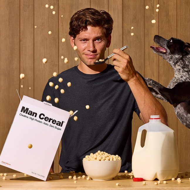 Man eating cereal with a dog and 'Man Cereal' packaging in the background